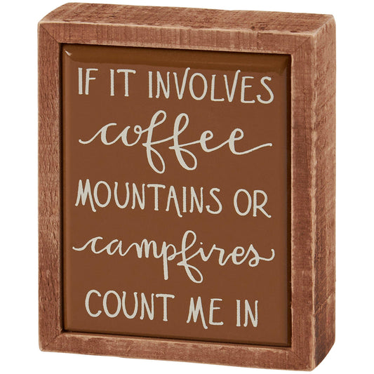 Wooden box with a brown background and white text reading 'If it involves coffee, mountains or campfires, count me in'.