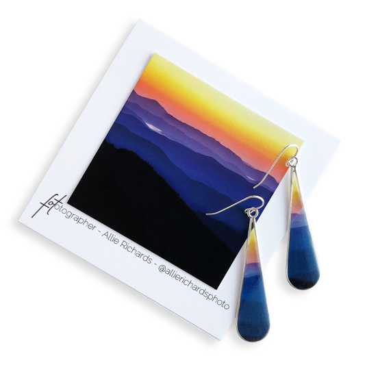 Colorful teardrop earrings on a card with a mountain landscape design.