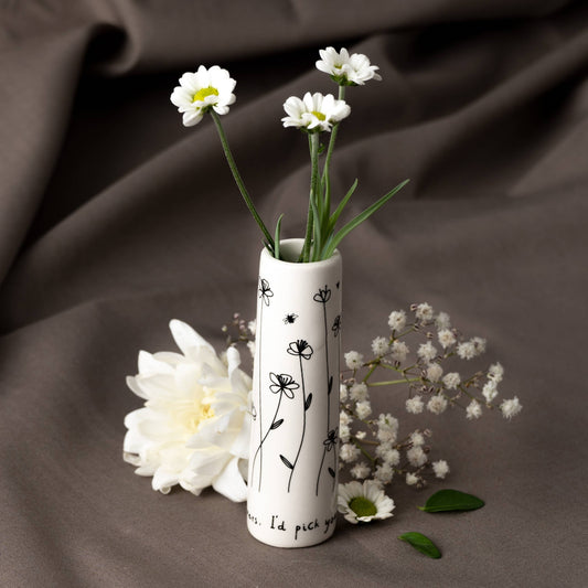 White vase with black floral patterns containing white flowers on a brown fabric background