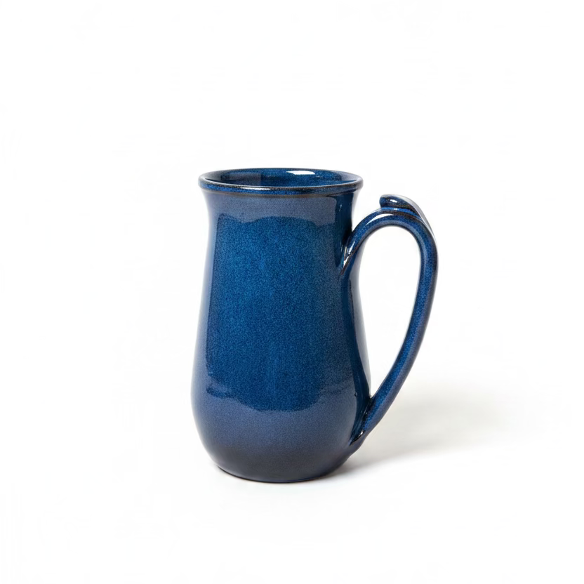 A handmade ceramic mug with a speckled deep blue glaze and a curved handle, and extra clay to grip top 